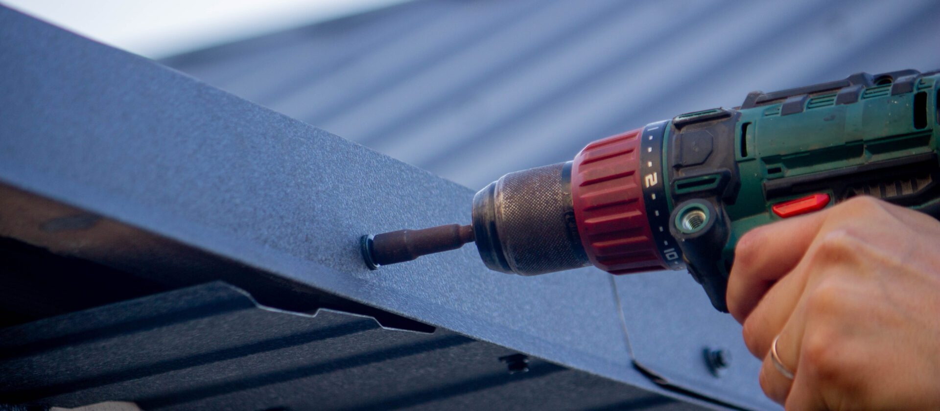 a man repairs the roof, tightens the self-tapping screw with a screwdriver. Selective focus